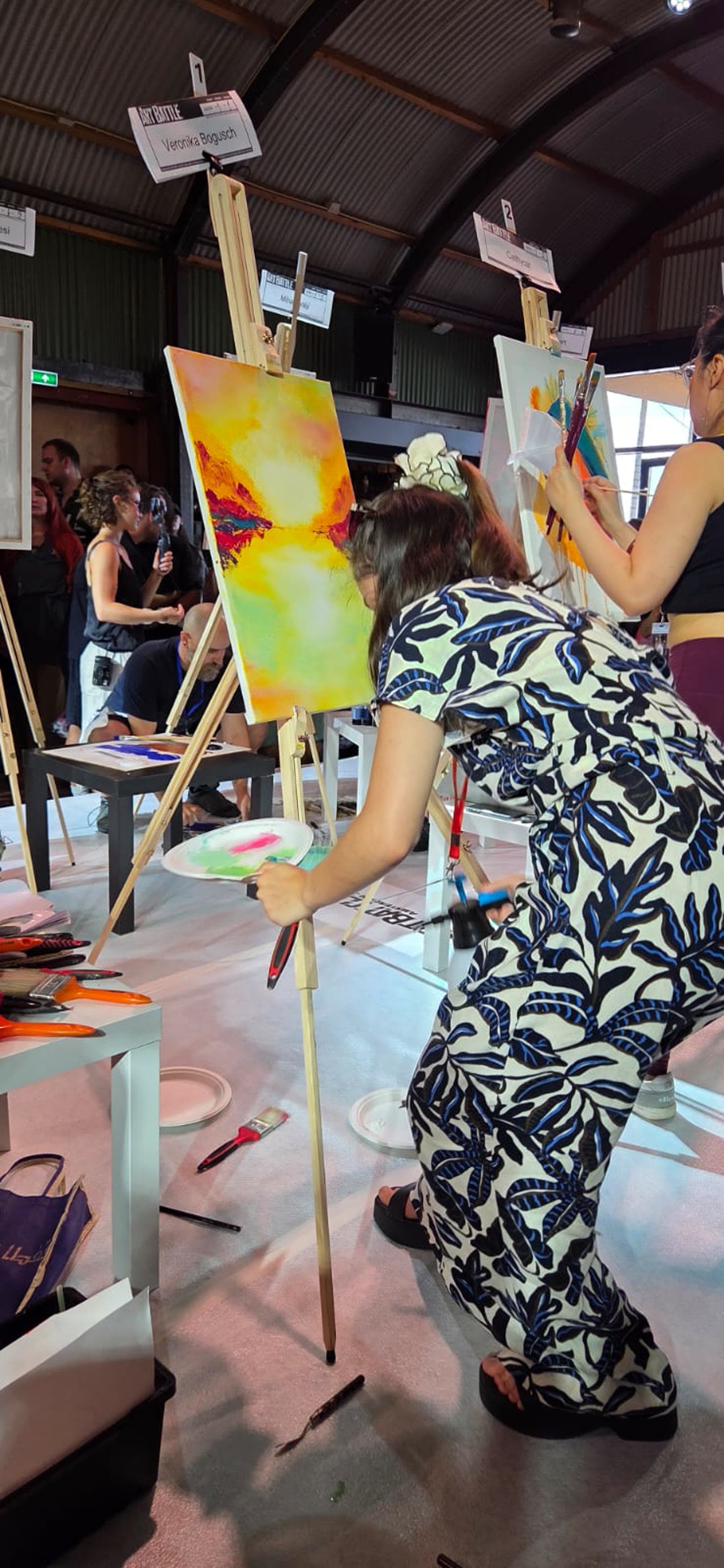 Veronika painting at an easel during the Art Battle, other competitors working behind her.