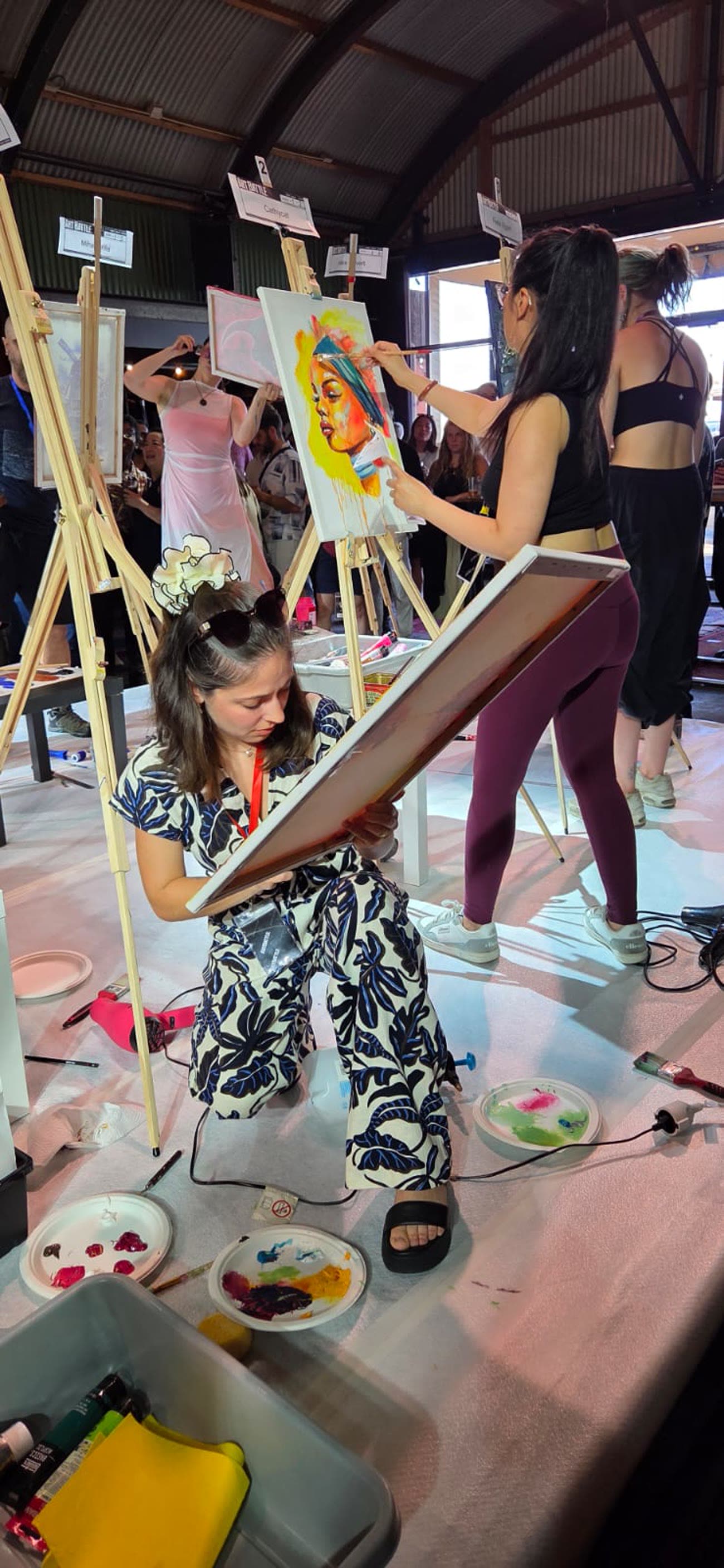 Veronika crouching over her canvas mid-competition, palettes on the floor around her.