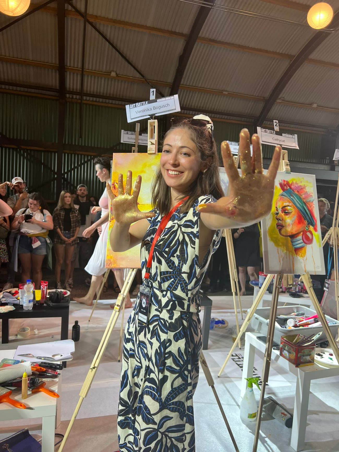 Veronika holding up two paint-covered hands in front of her finished canvas, laughing.