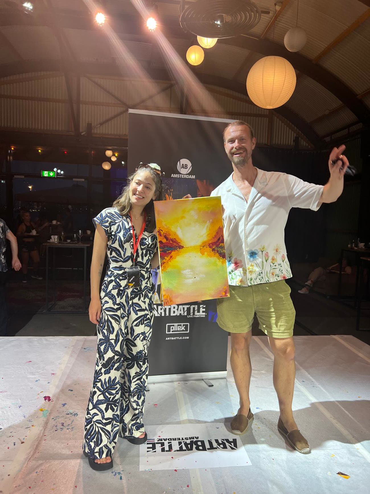 Veronika standing beside the man who bought her painting at the auction, holding it between them.