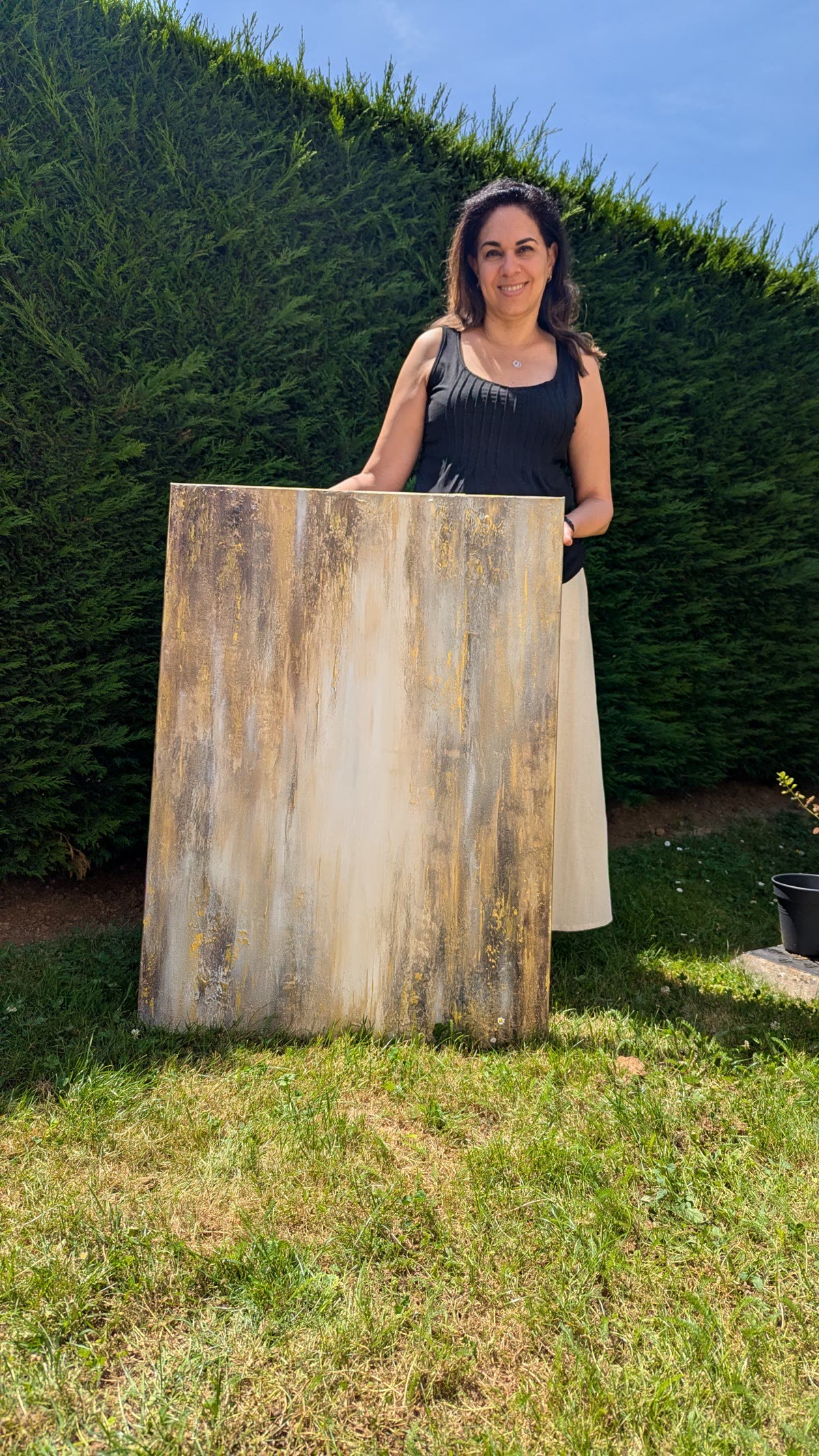 A collector holding her newly acquired painting in a garden.