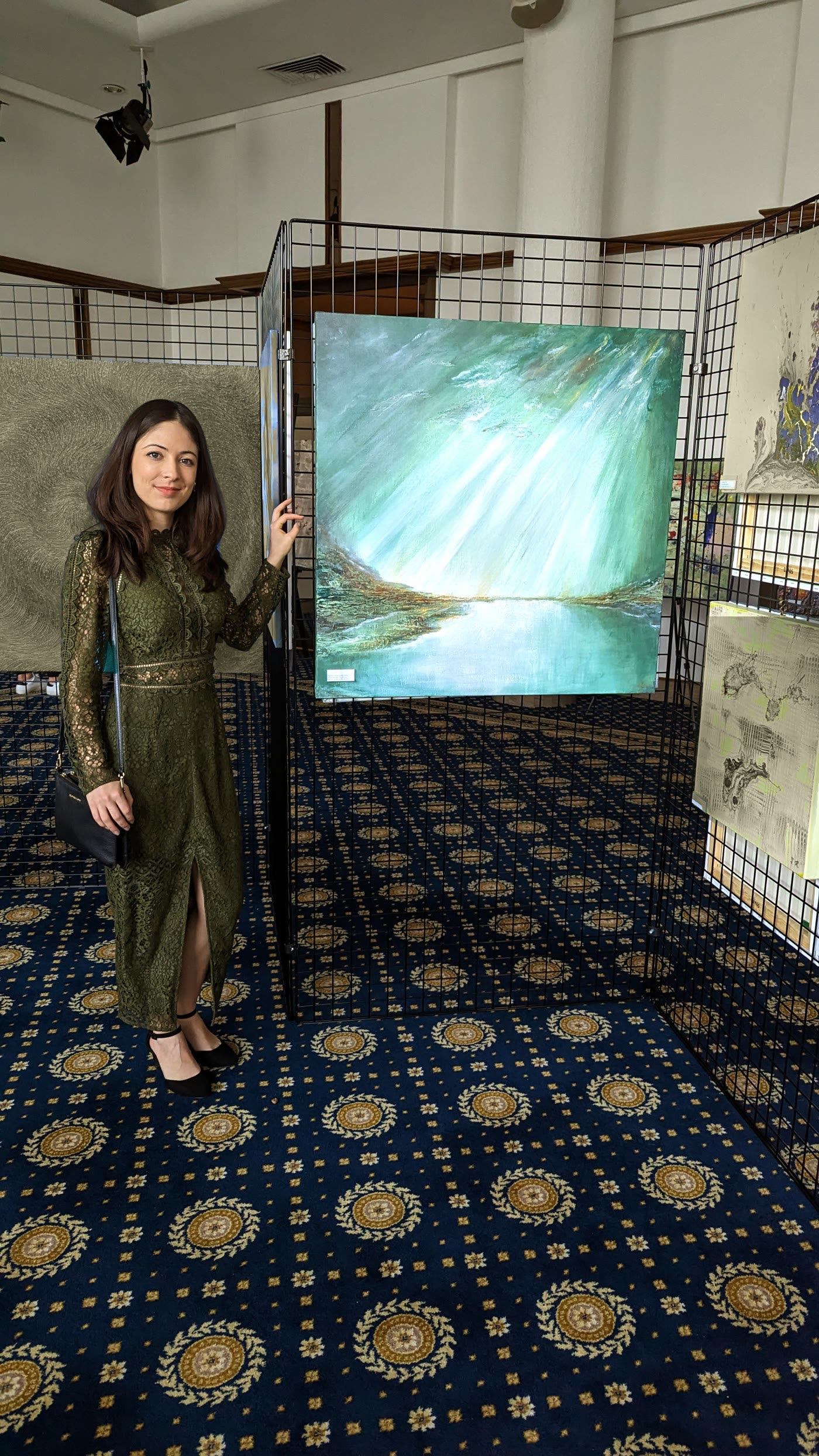 Veronika standing beside her turquoise painting at the exhibition in Lugano.