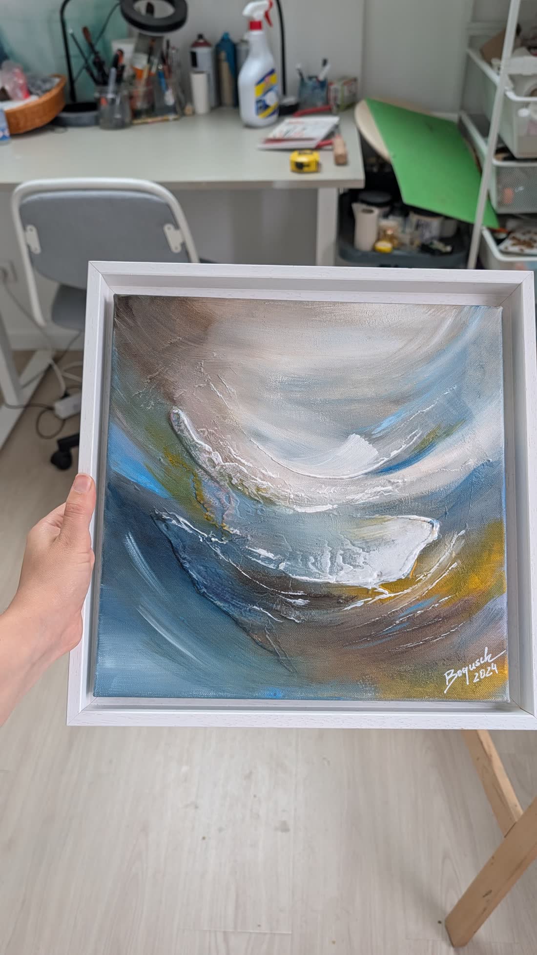 The framed painting held in the artist's hand in the studio.